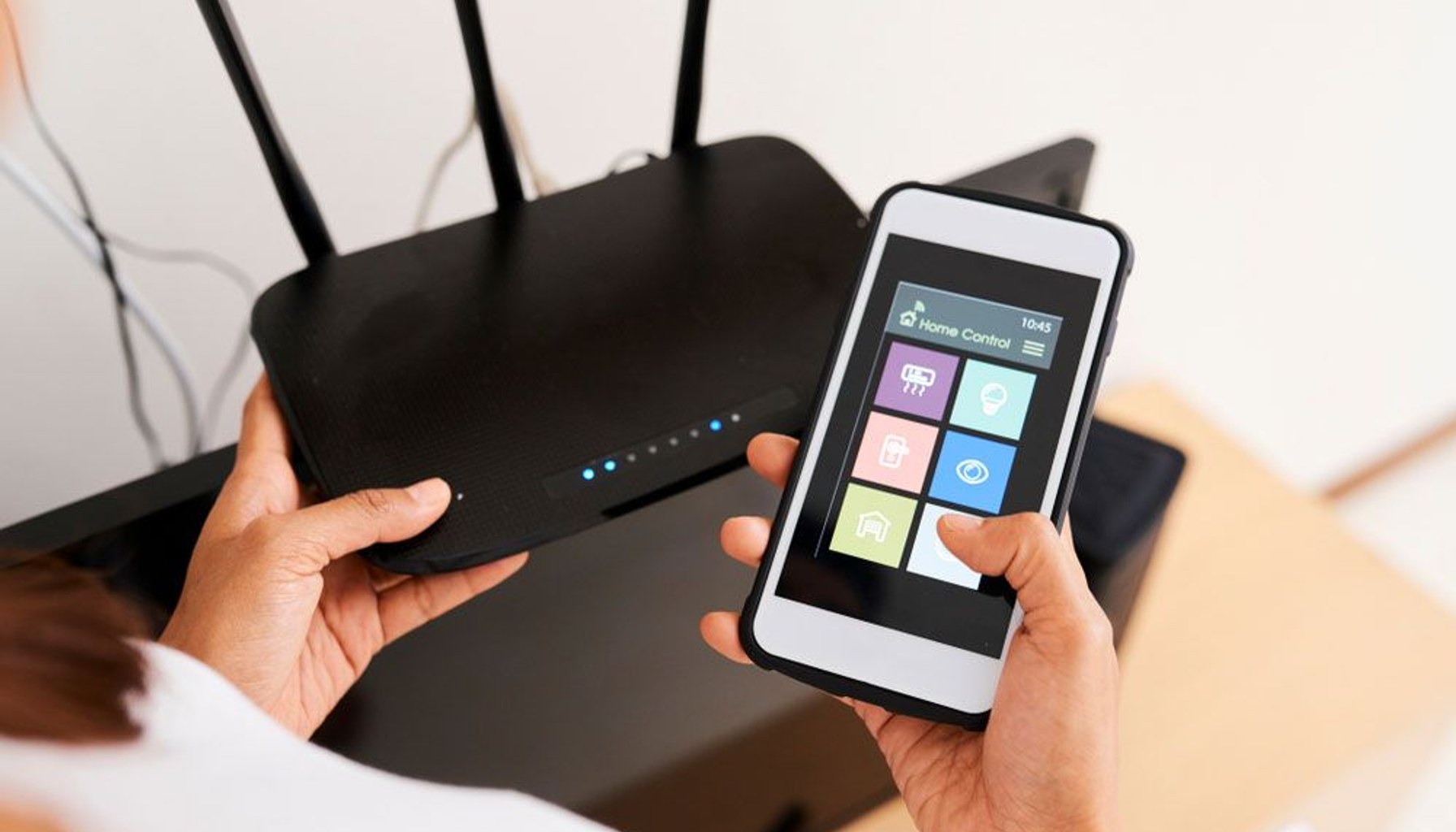 Person using smartphone app to control smart home while holding home wireless router.