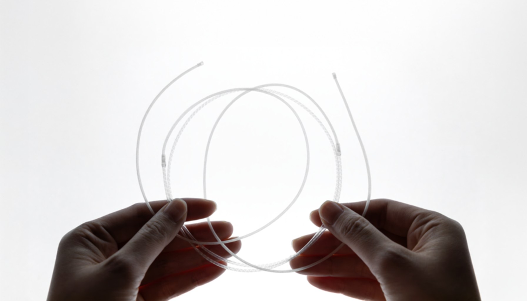 Two hands holding a coil of thin, transparent fiber tubing