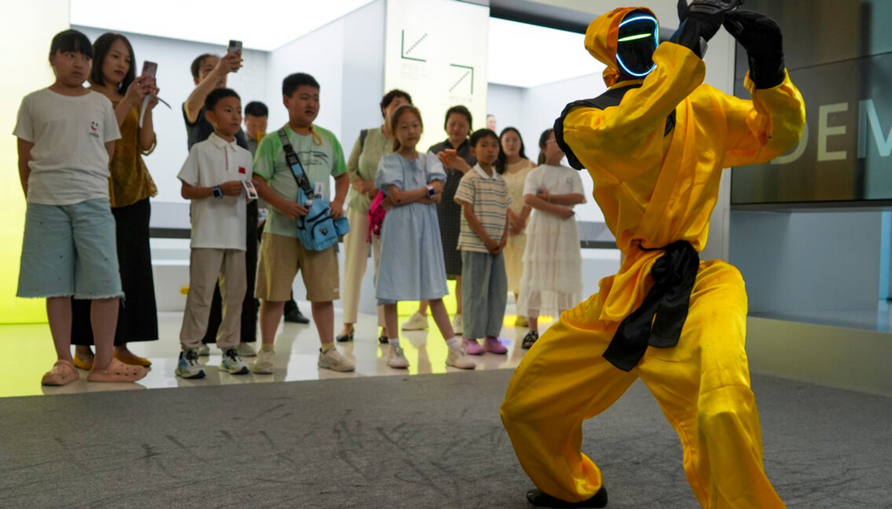 Children watch a martial arts performance by Unitree robots at a humanoid robot store on June 1, 2026 in Zhengzhou, Henan Province of China. The robot is wearing yellow martial arts clothing.