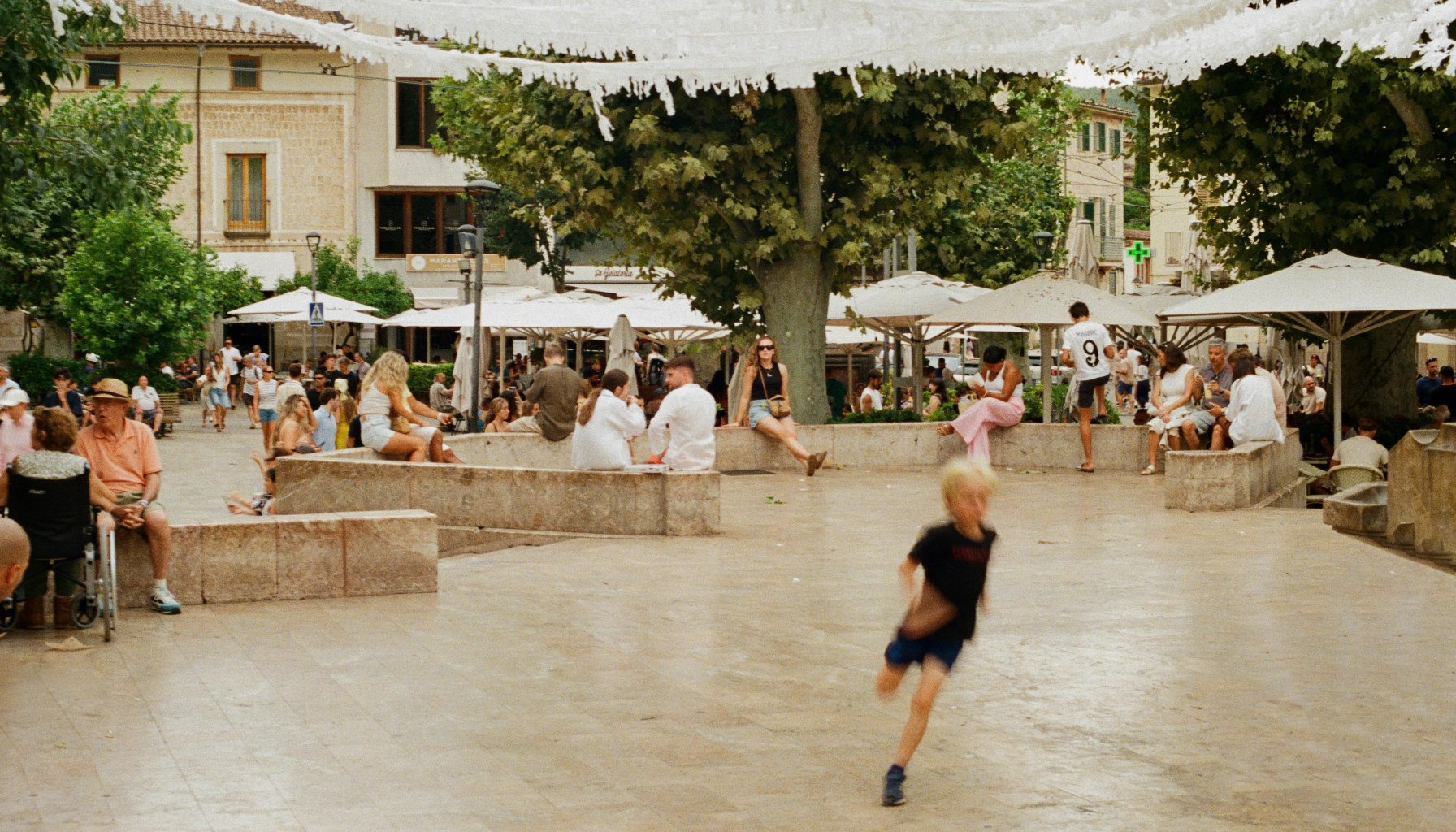An image of a child, blurred, running in the square of a town.